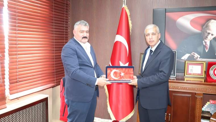İki kişi, Türk bayrağının önünde üzerinde ay yıldız bulunan bir plaketi birlikte tutuyor.