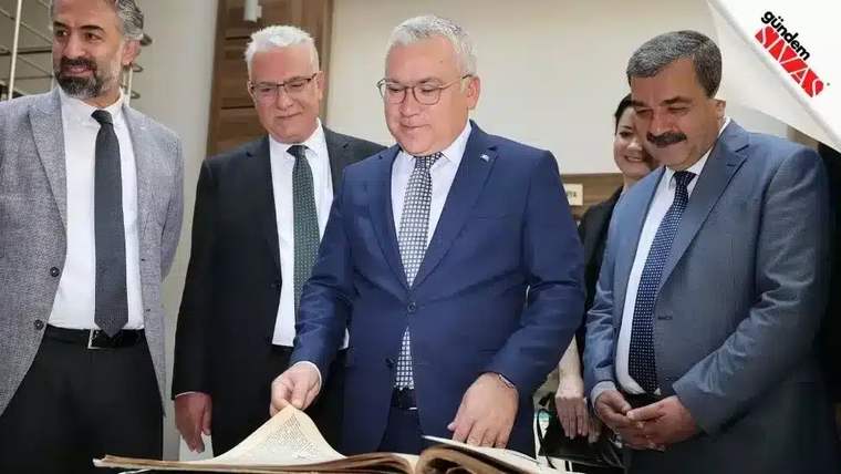 Bir grup insan, büyük bir kitabı inceliyor; ön planda bir kişi kitabı açmış.