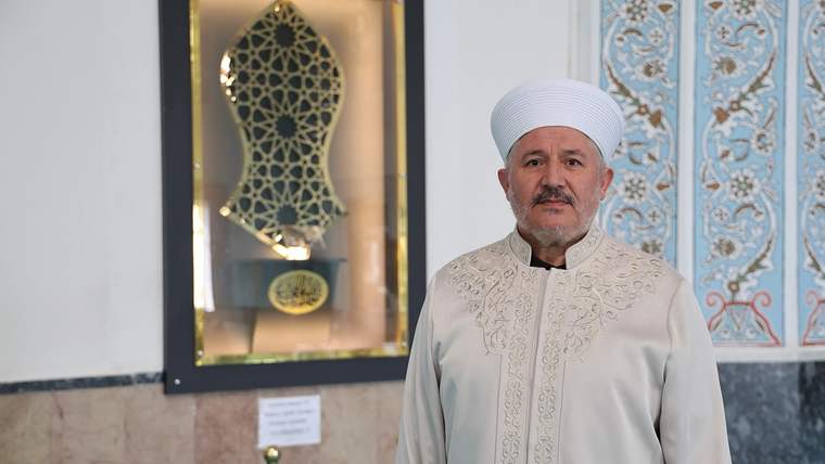 Beyaz sarık ve geleneksel kıyafet giymiş bir kişi, Sivas Paşa Camii içinde duruyor.