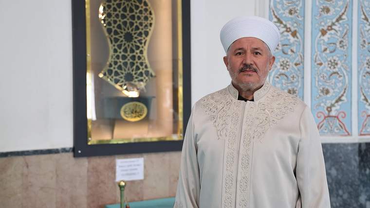 Beyaz sarık ve geleneksel kıyafet giymiş bir kişi, Sivas Paşa Camii içinde duruyor.