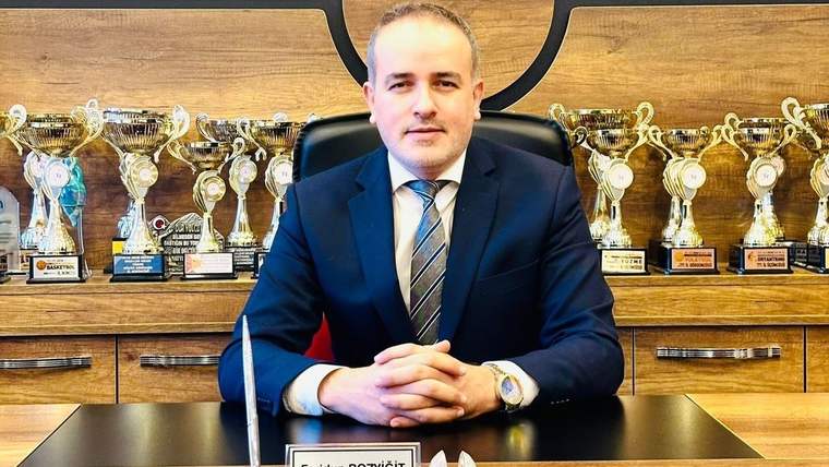 Bir masa başında oturan bir kişi, arkasında çeşitli kupalar ve ödüller var.