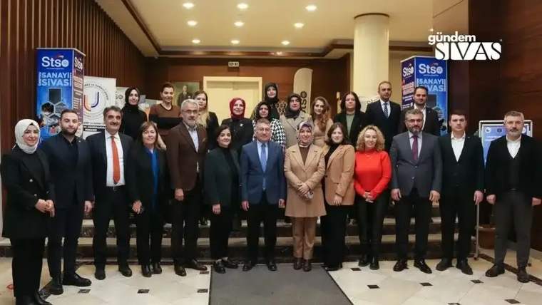 Lobi girişinde kadın ve erkeklerden oluşan bir grup, iki tanıtım panosunun önünde yan yana duruyor.