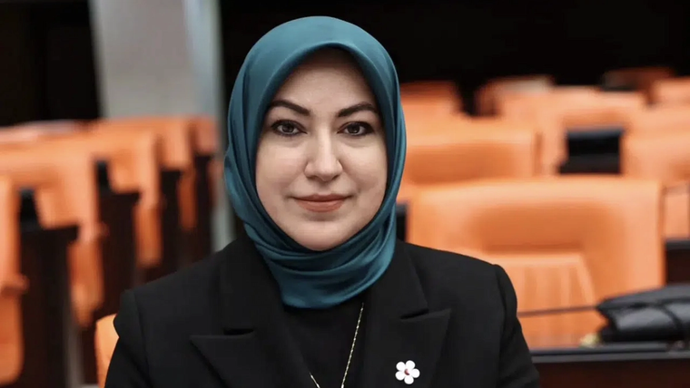 Kahverengi bir arka planda, başında başörtüsü olan bir kadın gülümsüyor. Önünde turuncu koltuklar var.