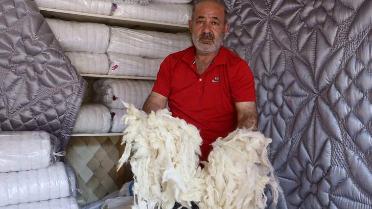 Kırmızı tişörtlü bir kişi, elinde yün parçaları tutarak bir odada oturuyor.