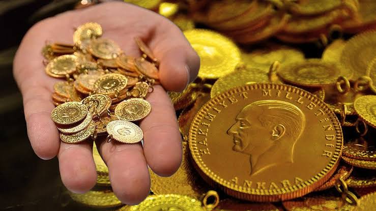 Bir elde çeşitli altın sikkeler, yanında büyük madalyon ve zincir parçaları bulunuyor.