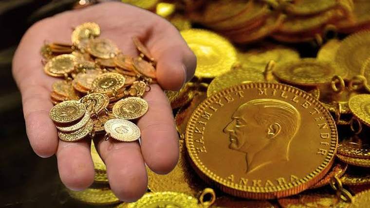 Bir elde çeşitli altın sikkeler, yanında büyük madalyon ve zincir parçaları bulunuyor.