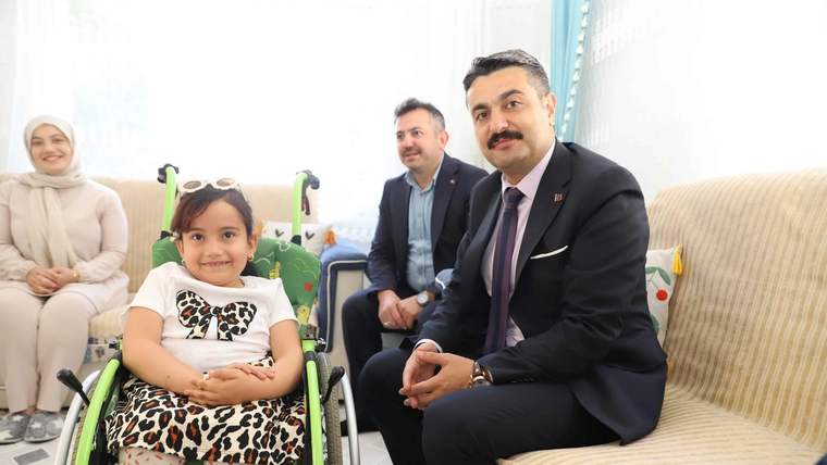 Bir kız çocuğu tekerlekli sandalyede otururken yanında takım elbiseli bir erkek ve iki yetişkin oturuyor.