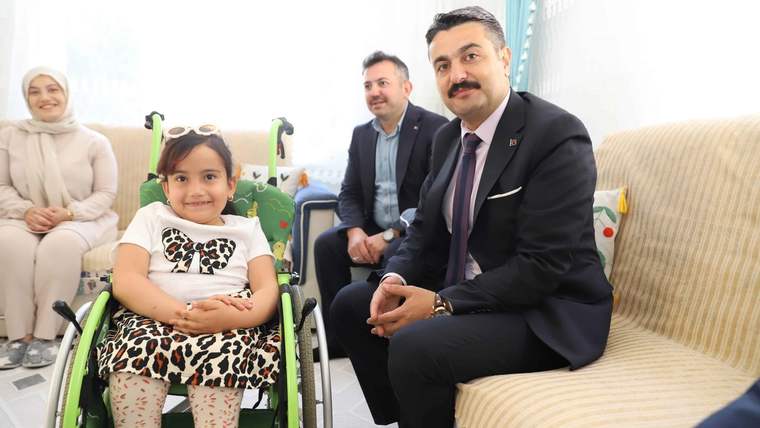 Bir kız çocuğu tekerlekli sandalyede otururken yanında takım elbiseli bir erkek ve iki yetişkin oturuyor.