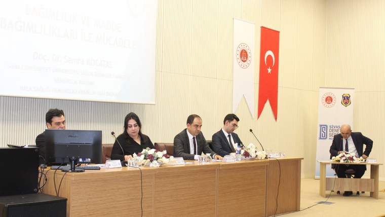 Toplantı salonunda dört kişi uzun masada oturuyor; Türk bayrakları ve kurum flamaları arkada yer alıyor.