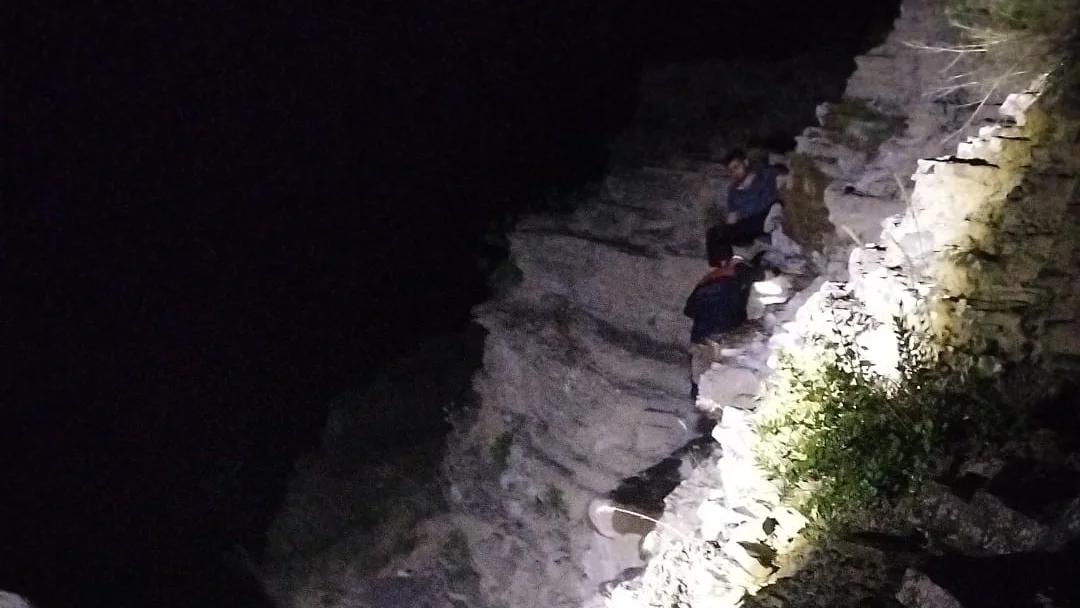 Karanlık bir ortamda kayalık bir alanda oturan birkaç kişi görünüyor.