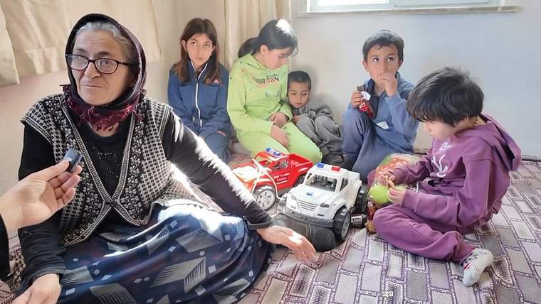 Başörtülü bir kadın, yerde oyuncak araçlarla oturan dört çocuk ve yanındaki iki çocuğun arasında görülüyor.