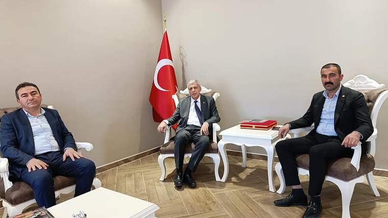 Türk bayrağının önünde, takım elbiseli üç kişi koltuklarda oturuyor; ortadaki kişinin yanında baston bulunuyor.