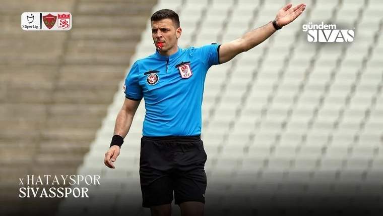 Mavi hakem forması giymiş bir hakem, elini yukarı kaldırarak işaret yapıyor.