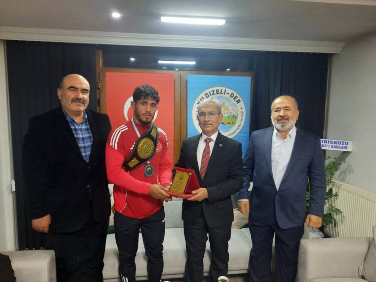 Dünya şampiyonu bir sporcu, ödülünü elinde tutarak dört kişiyle birlikte poz veriyor.