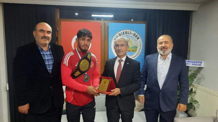 Dünya şampiyonu bir sporcu, ödülünü elinde tutarak dört kişiyle birlikte poz veriyor.