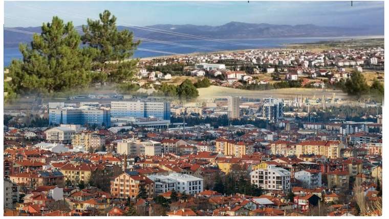 Kırmızı çatılı evler ve çok katlı binalardan oluşan kent, arka planda göl ve dağlarla görülüyor.