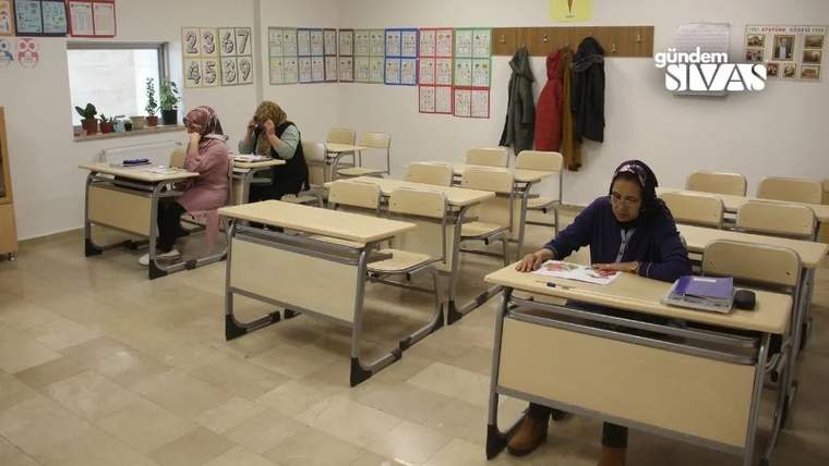 Sınıfta sıralarında oturan üç kadın, önlerindeki çalışma kitaplarına bakarak ders çalışıyor.