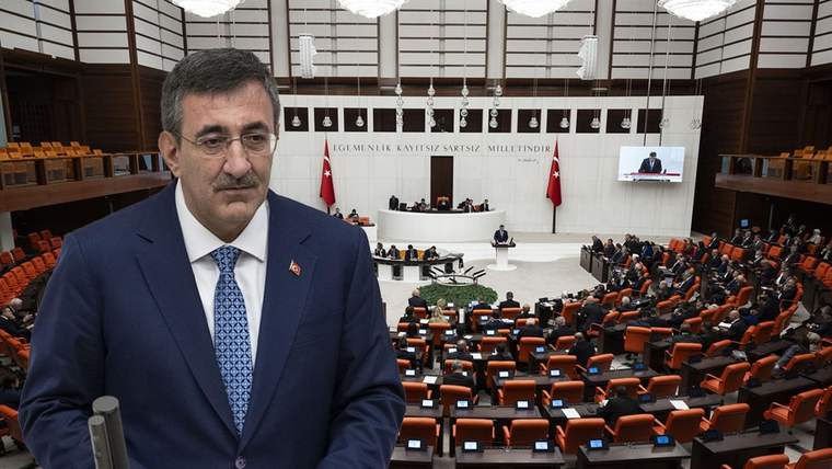 Takım elbiseli bir kişi kürsü önünde duruyor; arka planda Türkiye Büyük Millet Meclisi salonu görülüyor.