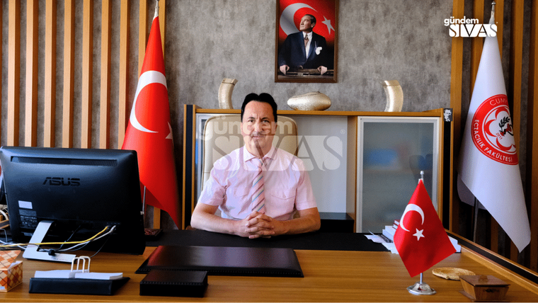 Bir masa başında oturan bir kişi, arkasında Türk bayrağı ve Atatürk portresi var.