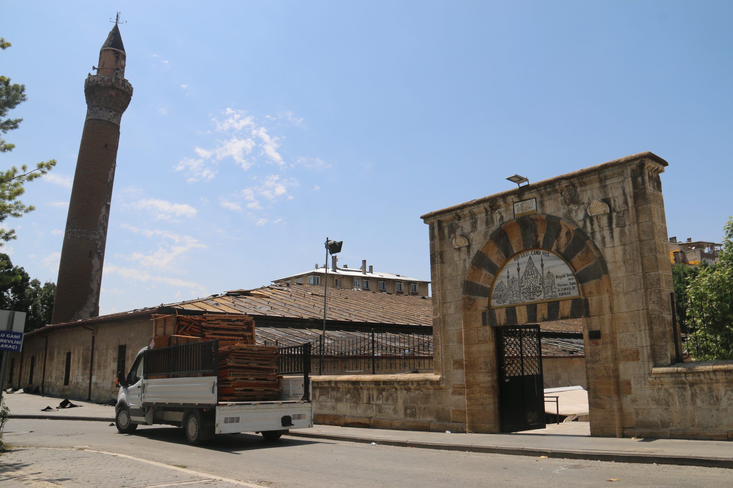Taş kemerli giriş ve minaresi görünen tarihi caminin önünde küçük bir kamyonet duruyor.