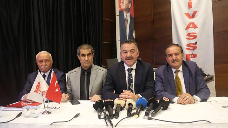 Dört kişi, masanın arkasında oturuyor; masada mikrofonlar ve su bardakları var.
