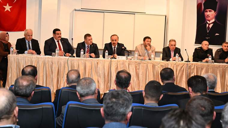 Toplantı salonunda masada oturan kişiler, önlerindeki dinleyici topluluğuna karşı sıralanıyor.