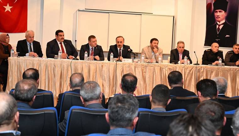Toplantı salonunda masada oturan kişiler, önlerindeki dinleyici topluluğuna karşı sıralanıyor.