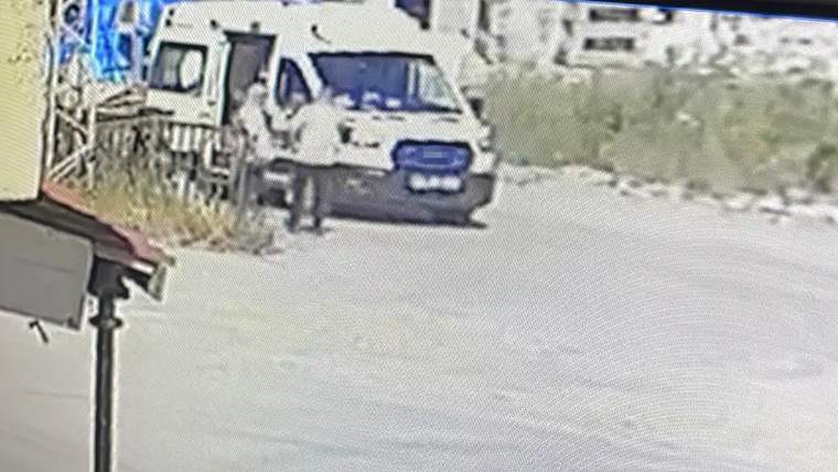 Beyaz bir ambulans, yol kenarında duruyor. Arka planda yeşil bitki örtüsü ve binalar görünmekte.