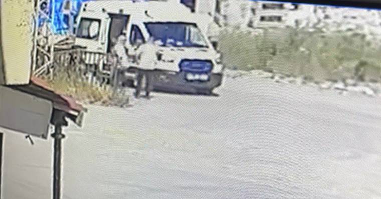 Beyaz bir ambulans, yol kenarında duruyor. Arka planda yeşil bitki örtüsü ve binalar görünmekte.