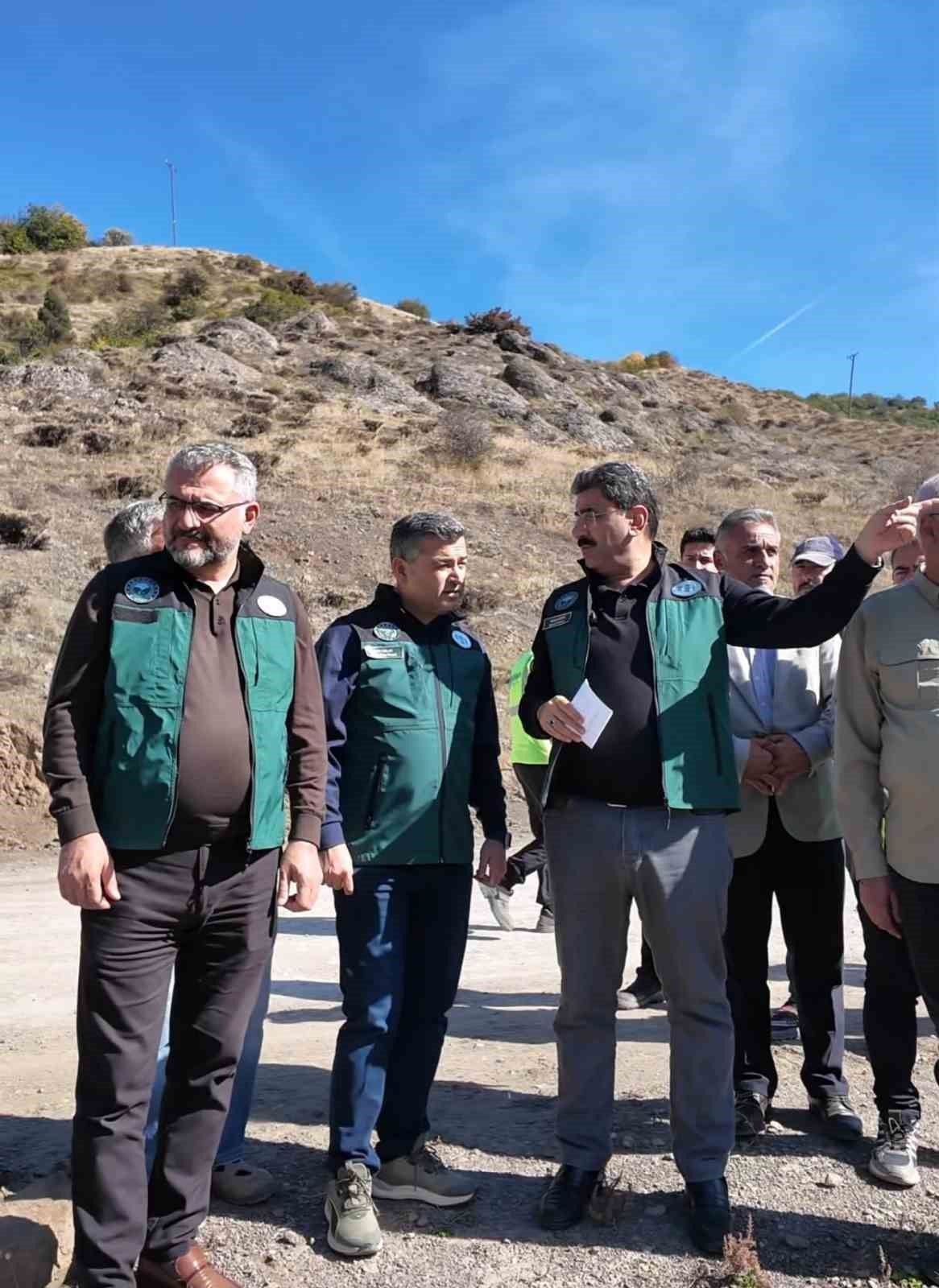 Kayalık yamaç önünde yeşil yelekli bir grup duruyor; öndeki kişilerden biri sağ tarafı işaret ediyor.