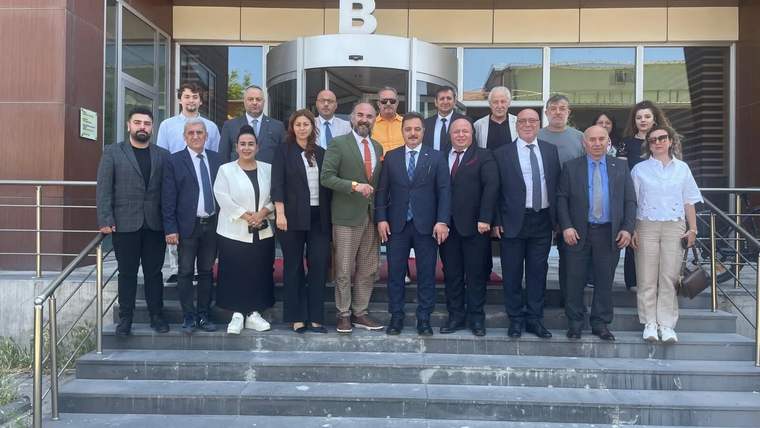 Girişinde büyük B harfi bulunan binanın merdivenlerinde, kalabalık bir grup yetişkin birlikte duruyor.
