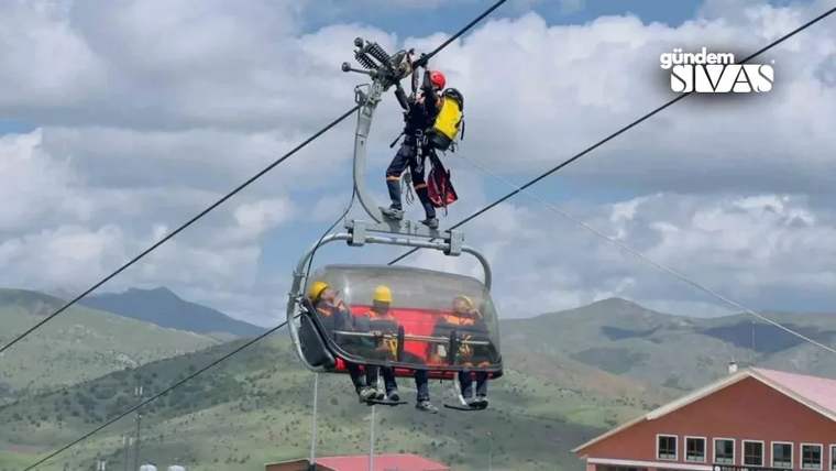 Teleferik hattında çalışan bir kişi, teleferik kabininde oturan üç kişiye eğitim veriyor.