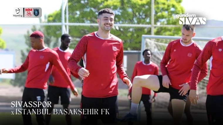 Kırmızı formalar giyen futbolcular, açık sahada ısınma hareketleri yaparken ortadaki oyuncu gülümsüyor.