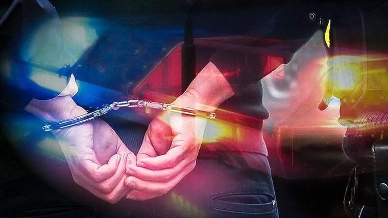 Kelepçeli eller, arka planda mavi ve kırmızı ışıklar yanan bir polis aracı görünmekte.