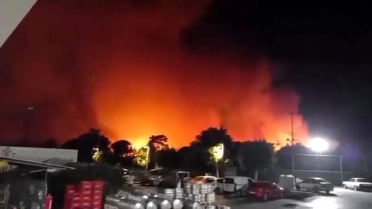 Ağaçların arkasında yükselen yoğun duman ve alevler, gece gökyüzünü turuncu renge boyuyor.