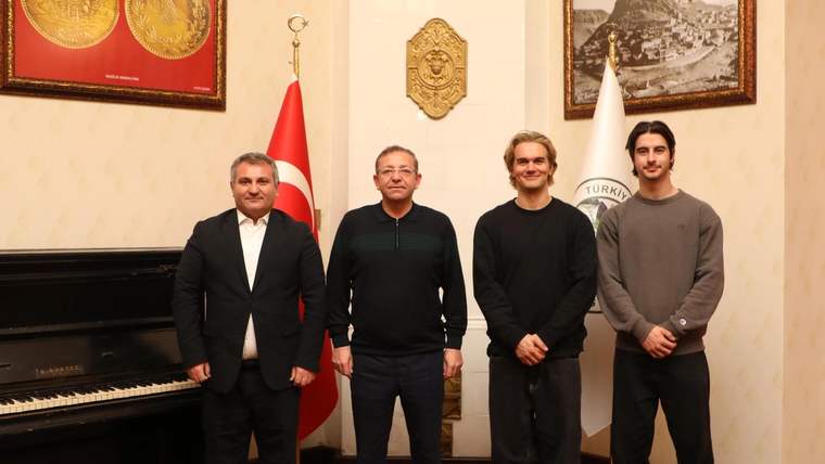 Dört kişi, bir odada yan yana duruyor; arka planda Türk bayrağı ve Kars manzarası olan bir tablo var.