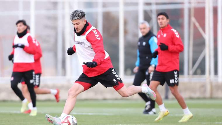 Kırmızı formalı futbolcuların antrenman sahasında çalıştığı, öndeki oyuncunun topa vurduğu an