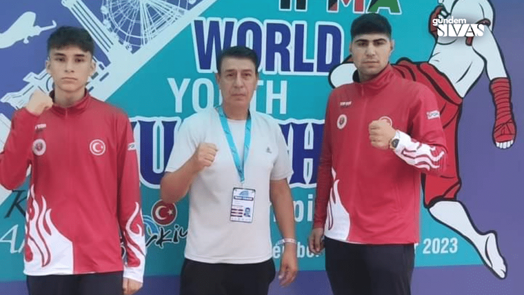 Kırmızı eşofmanlı iki genç ile beyaz tişörtlü bir kişi, spor etkinliği pankartı önünde duruyor.