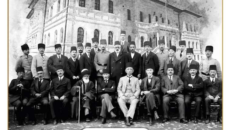 Tarihi bir binanın önünde, çoğu takım elbiseli ve fesli kalabalık bir grup birlikte poz veriyor.