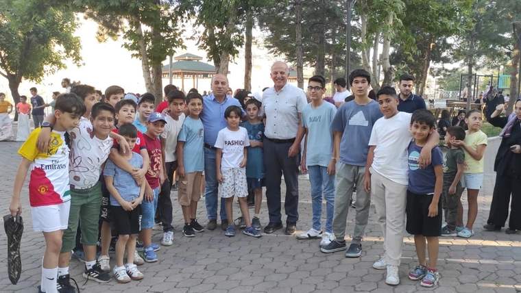 Ağaçlık bir alanda, farklı yaşlarda çocuklar ve iki yetişkin birlikte poz veriyor.