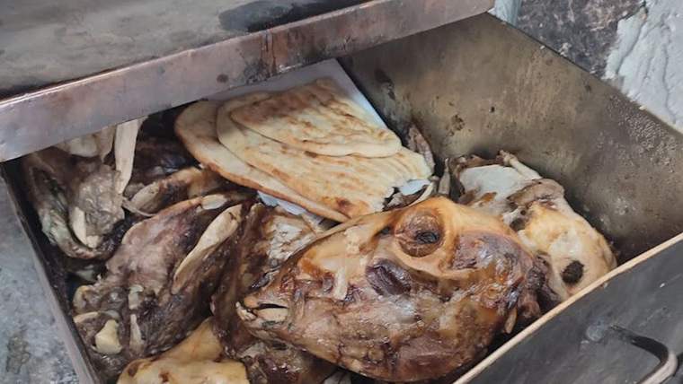 Metal bir haznede, pişmiş hayvan başı ve et parçalarıyla birlikte yassı ekmekler görülüyor.