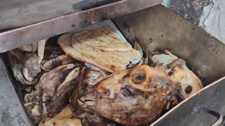 Metal bir haznede, pişmiş hayvan başı ve et parçalarıyla birlikte yassı ekmekler görülüyor.