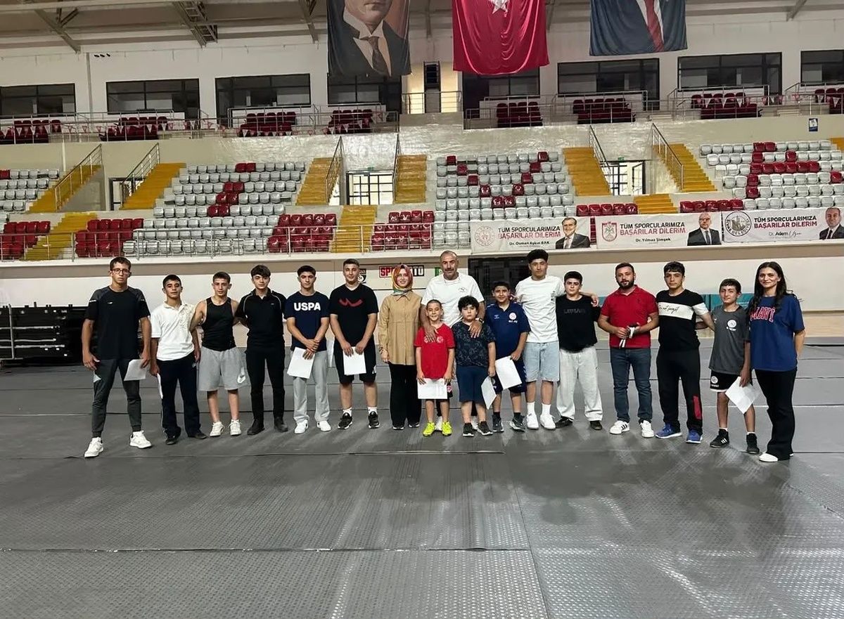 Spor salonunun minderli alanında, farklı yaşlardan bir grup genç ve yetişkin yan yana duruyor.