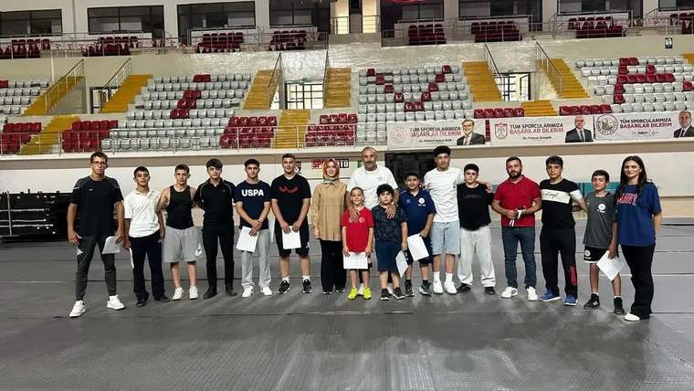 Spor salonunun minderli alanında, farklı yaşlardan bir grup genç ve yetişkin yan yana duruyor.