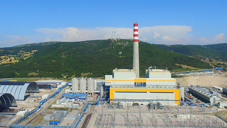 Büyük bir santral binası, arka planda yeşil dağlarla çevrili.