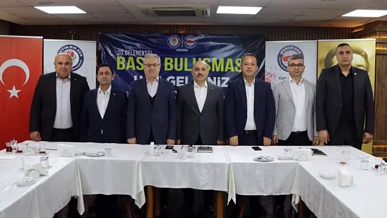 Toplantı salonunda altı erkek, üzerinde “Basın Buluşması” yazan pankartın önünde masa arkasında duruyor.