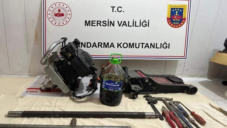 Mersin Valiliği Jandarma Komutanlığı tabelası önünde metal arama cihazı, bidon, çubuklar ve el aletleri duruyor.