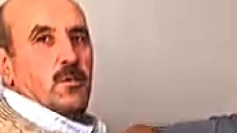 Bir kişi, odada otururken kameraya bakıyor.