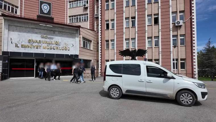 Üzerinde Sivas Valiliği ve İl Emniyet Müdürlüğü yazan bina önünde beyaz bir minibüs ve insanlar görülüyor.