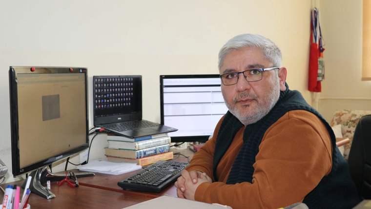 Bir masa başında oturan, gözlük takan bir kişi, bilgisayar ekranlarına bakıyor.